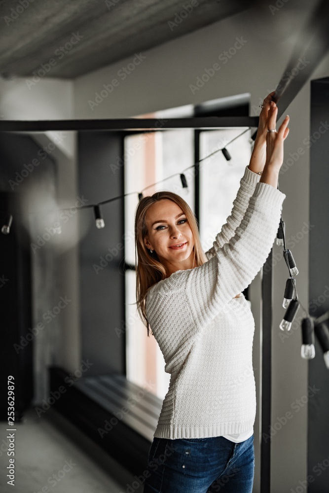 A beautiful girl in blue jeans and a white sweater posing in a metal cube and at the window. A beautiful girl in blue jeans and a white sweater posing in a metal cube and at the window.
