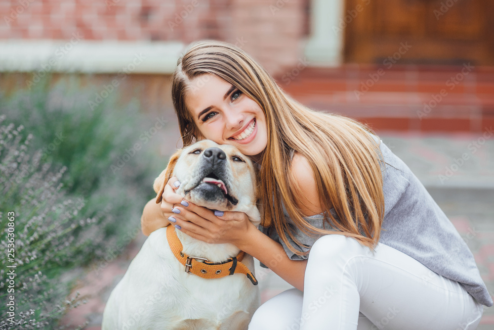 Young girl with retriever on walk in summer park. Attractive smiling woman hugging her labrador retriever and looking into the camera. Young girl with retriever on walk in summer park. Attractive smiling woman hugging her labrador retriever and looking into the camera.
