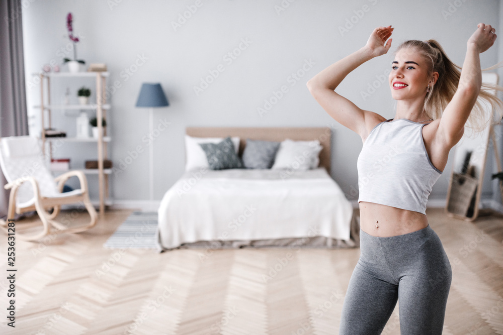 Young sporty woman doing morning exercise standing in living room. Young sporty woman doing morning exercise standing in living room.