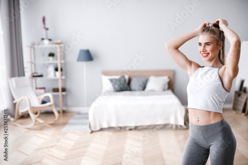 Young sporty woman doing morning exercise standing in living room.