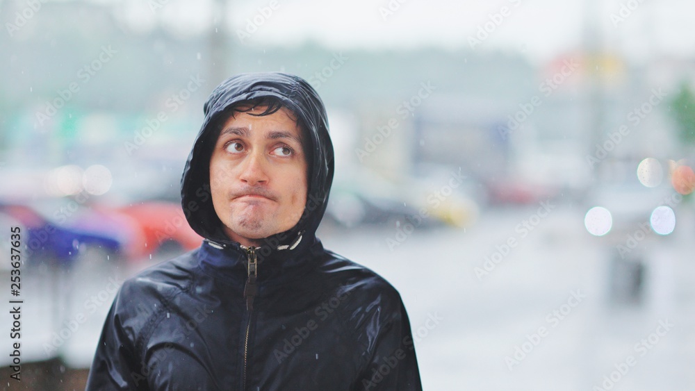Portrait of a young man in a jacket with a hood in the rain on blurred background city street, close-up Portrait of a young man in a jacket with a hood in the rain on blurred background city street, close-up