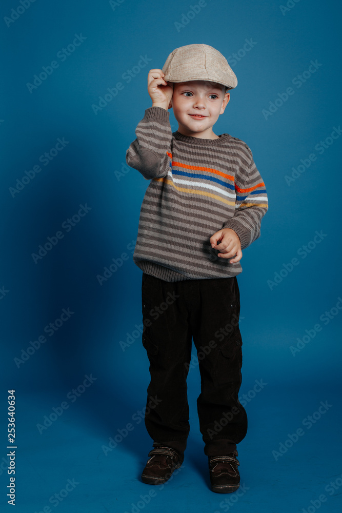 A little boy in a cap is posing and smiling.