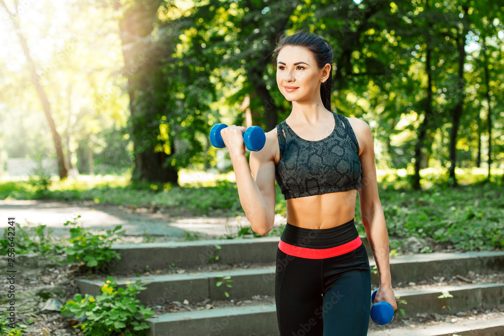 Young woman exercising with dumbbells at the park. Female fitness model working out outdoor. Concept of healthy lifestyle. Young woman exercising with dumbbells at the park. Female fitness model working out outdoor. Concept of healthy lifestyle.