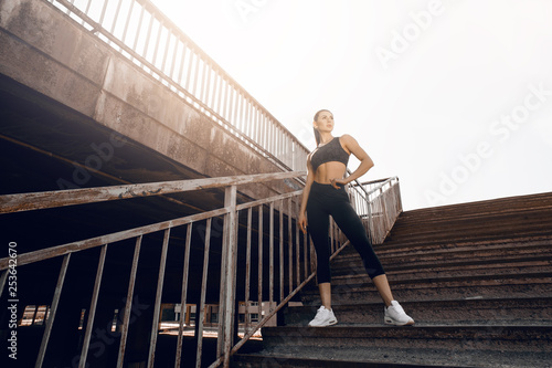 Young sexy woman jogger athlete training on road. Concept of healthy lifestyle. Female fitness model working out outdoor in city on the steps.