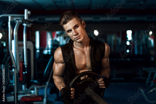 Muscular model sports young man exercising in gym with dumbbell. Portrait of sporty healthy strong muscle. Fitness trainer. Sport workout bodybuilding motivation concept. Sexy torso. © KDdesignphoto