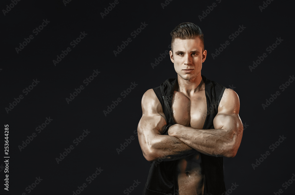 Fototapeta premium Muscular model young man on dark background. Strong brutal guy showing his biceps triceps, flexing his muscles. Sexy naked torso, six pack abs. Sport workout bodybuilding healthy lifestyle concept.