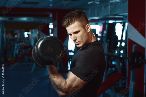 Muscular model sports young man exercising in gym with dumbbell. Portrait of sporty healthy strong muscle. Fitness trainer. Sport workout bodybuilding motivation concept.