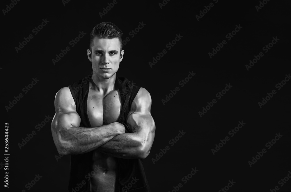 Muscular model young man on dark background. Strong brutal guy showing his biceps triceps, flexing his muscles. Sexy naked torso, six pack abs. Sport workout bodybuilding healthy lifestyle concept.