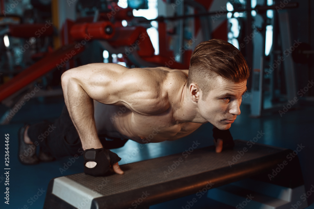 Muscular model sports young man exercising in gym. Guy doing push-ups. Portrait of sporty healthy strong muscle. Fitness trainer. Sport workout bodybuilding motivation concept. Muscular model sports young man exercising in gym. Guy doing push-ups. Portrait of sporty healthy strong muscle. Fitness trainer. Sport workout bodybuilding motivation concept.