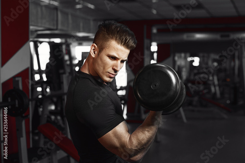 Muscular model sports young man exercising in gym with dumbbell. Portrait of sporty healthy strong muscle. Fitness trainer. Sport workout bodybuilding motivation concept.