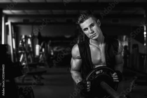 Muscular model sports young man exercising in gym with dumbbell. Black and white portrait of  strong muscle. Fitness trainer. Sport workout bodybuilding motivation concept. Sexy torso.