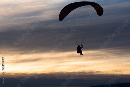 A man paragliding down a mountain against a cloudy sunset in winter