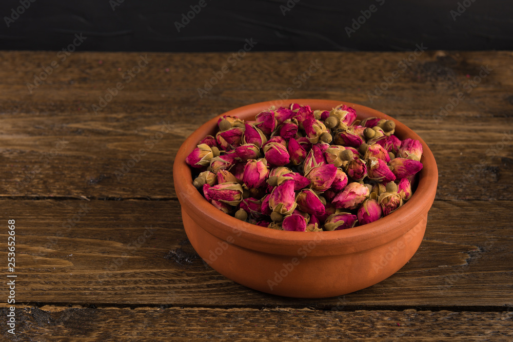 tea rose buds in a clay pot isolated on wooden table on black background tea rose buds in a clay pot isolated on wooden table on black background