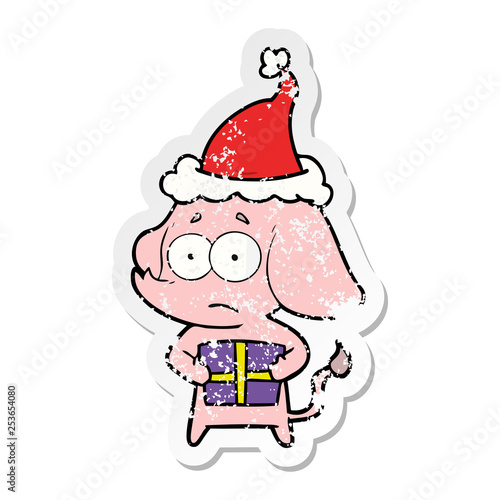 distressed sticker cartoon of a unsure elephant with christmas present wearing santa hat