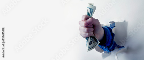 Obraz na plátne Fist full of paper money dollars, punching through a wall as symbol of purposefu