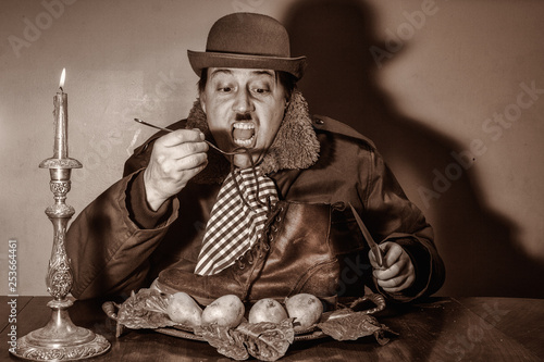 Poverty stricken, bankrupt, poor Caucasian male with mustache ,eating a boot by candle light , in a dirty , cold room ,dressed as Charlie Chaplin type character ,wearing a hat.