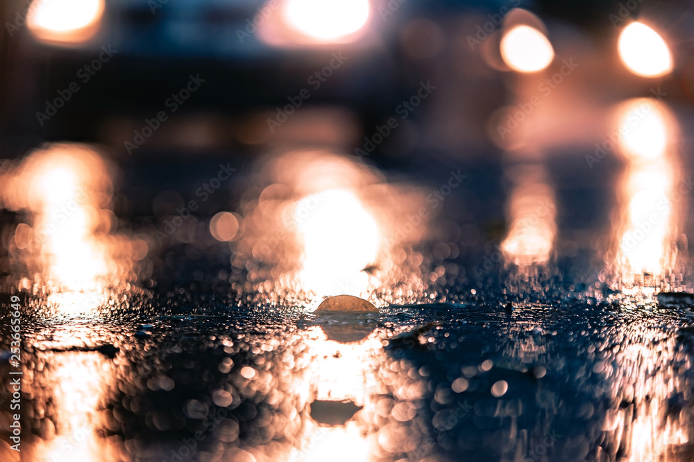 Night road blurred. Rain drops rippling in a puddle on a dark, rainy day, close up with soft selective focus . Water splashes, spills on roadway