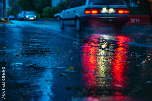 Motion car in rain with selective focus, color toned. Night road blurred, in the dark while heavy raining. Back light of car on raining road, light reflected on road. View from the level of asphalt