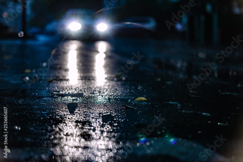 Motion car in rain, water spray. Night road blurred, headlight of car in the dark while heavy raining. Rain in the city. Road, pavement, car in rain