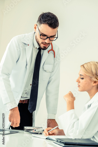 Young female doctor at hospital office having conversation talking with another male doctor standing beside the table. Concept of medical healthcare professional team. photo