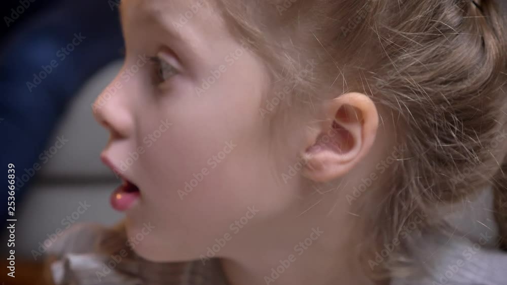 Close-up portrait of small caucasian girl with braids showing her amusement by opening her mouth into camera in cosy home atmosphere. Close-up portrait of small caucasian girl with braids showing her amusement by opening her mouth into camera in cosy home atmosphere.
