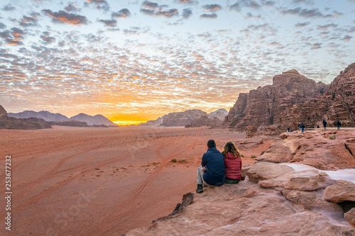 Фотография A young couple is watching at sunrise over wadi rum desert in Jordan