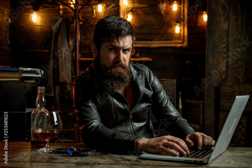 Portrait of a handsome man with beard. Brutality and masculine concept. Barbershop, shaving.Macho is drinking by his laptop. Deep look. Eye contact.