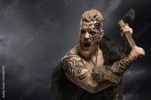 Medieval warrior berserk Viking with tattoo and in skin with axe attacks enemy. Close-up portrait photo