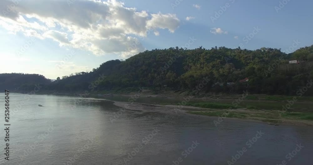 Forward aerial drone view of lush mountain range with view of monk children playing on the river banks of Mekong river. Forward aerial drone view of lush mountain range with view of monk children playing on the river banks of Mekong river.