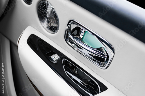 Door handle with power window control buttons of a luxury passenger car. White perforated leather interior with stitching and natural wood panel. Modern car interior details. Car detailing. Car inside © Aleksei