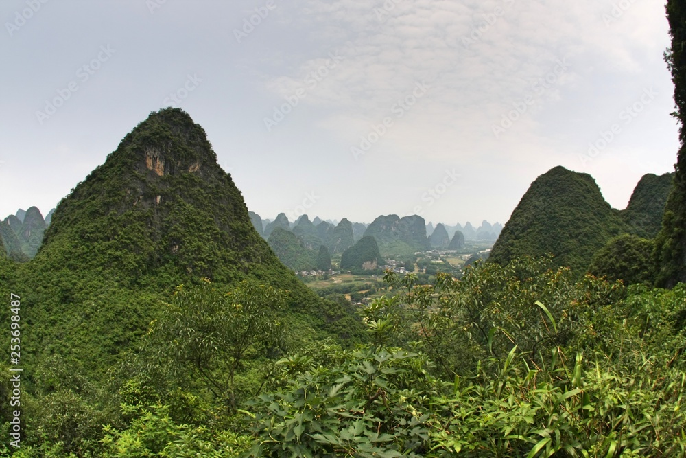 Karst peaks with green grass, tree and plant growth in Yangshuo, China with smog in air under grey sky