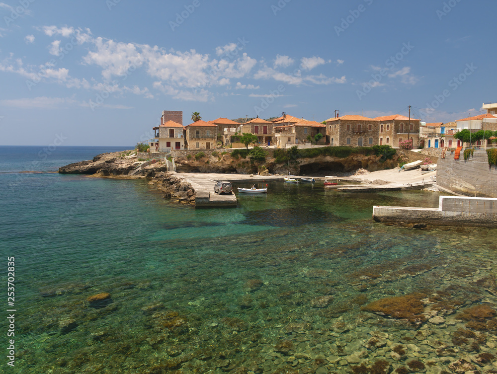 Crystal clear water beach with rocks and stone village houses  under day light in Mani, Greece.