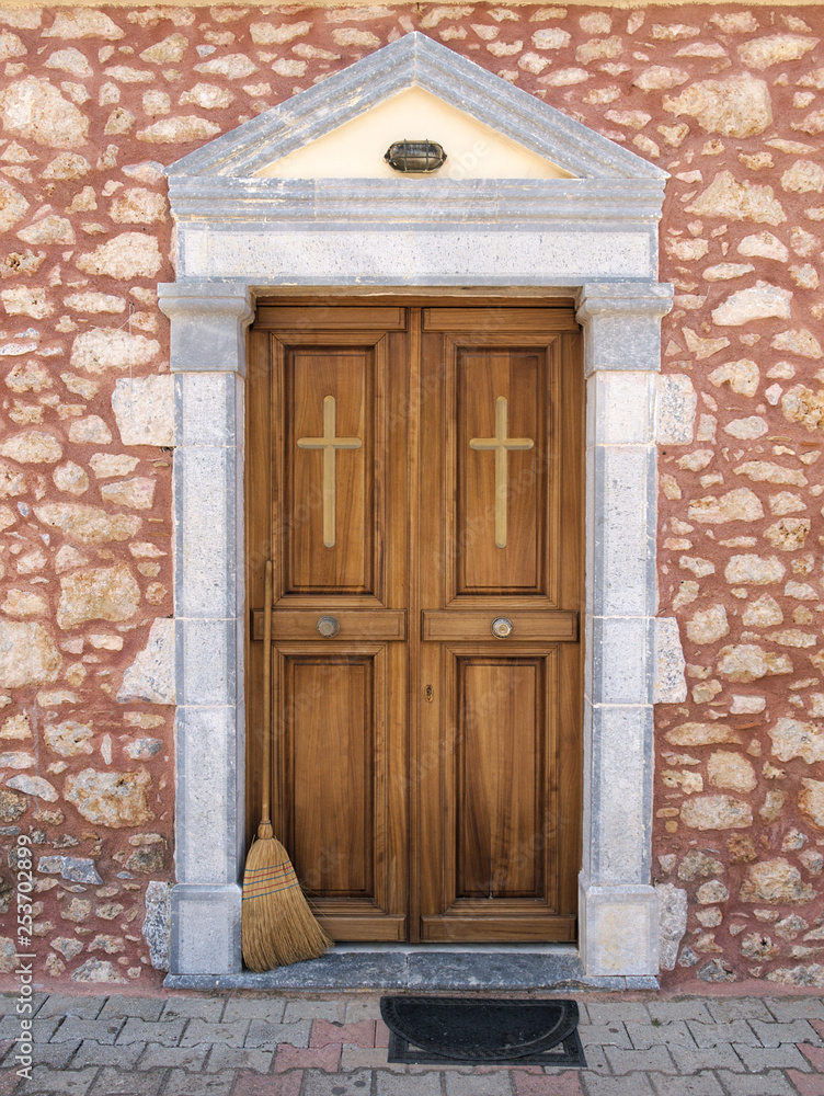 Beautiful clean wooden church door with crosse  on a stone wall and a hay broom with wooden handle.