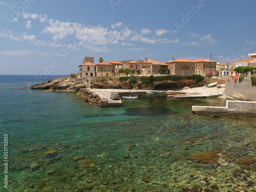 Crystal clear water beach with rocks and stone village houses  under day light in Mani  Greece.