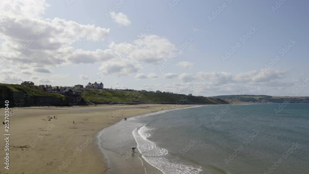 Beautiful beach in Whitby, UK with a sweeping wide sandy beach lined by cliffs and calm surf. Popular tourist destination in North Yorkshire. Warm summer sky and homes overlooking the sea. Beautiful beach in Whitby, UK with a sweeping wide sandy beach lined by cliffs and calm surf. Popular tourist destination in North Yorkshire. Warm summer sky and homes overlooking the sea.