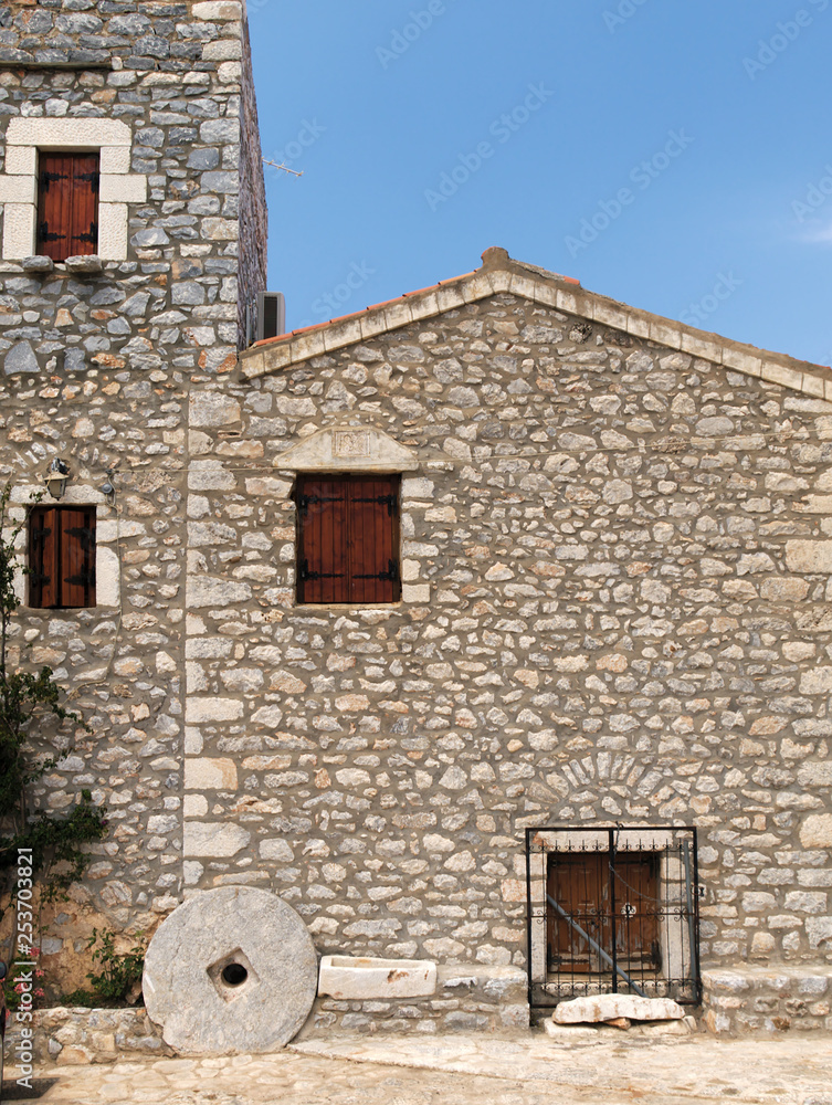 Traditional stone house with wooden windows and decorative millstone in a Greek village in Mani.