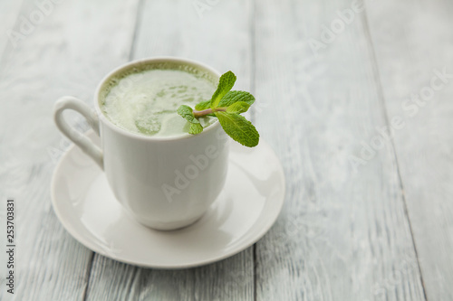 cup of hot matcha green tea with branch of mint on a grey background