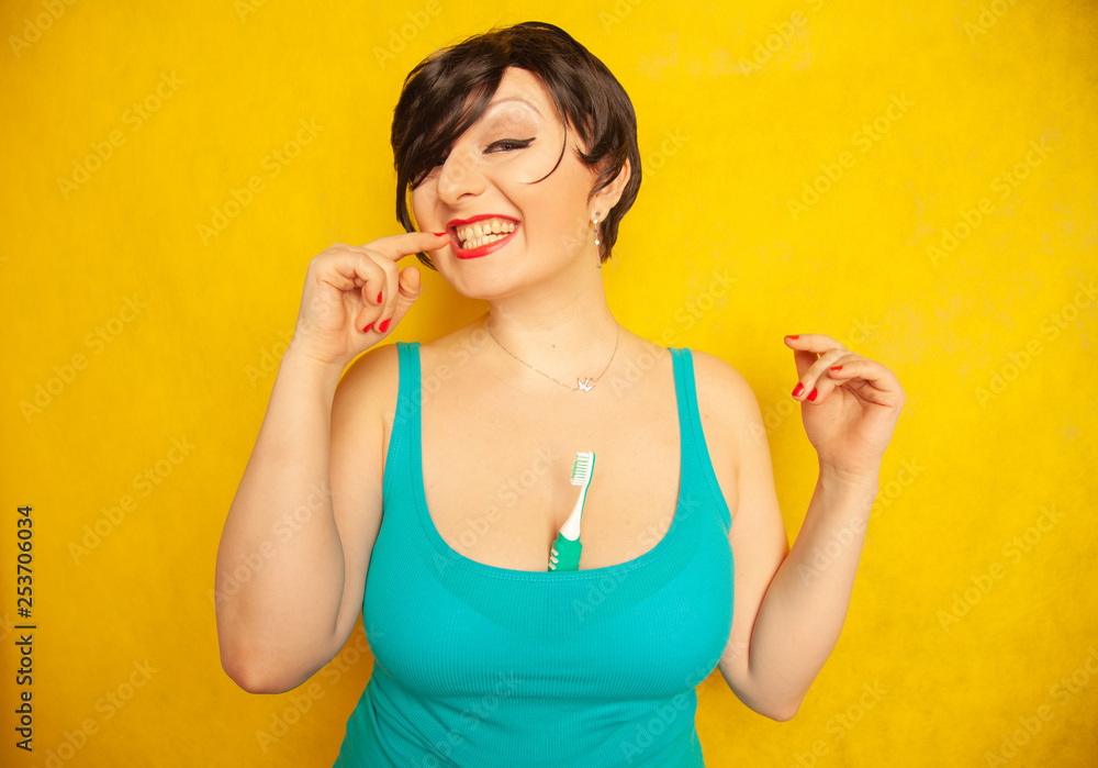 smiling girl with short hair and a curvy figure stands with a toothbrush in her hands on yellow solid studio background smiling girl with short hair and a curvy figure stands with a toothbrush in her hands on yellow solid studio background