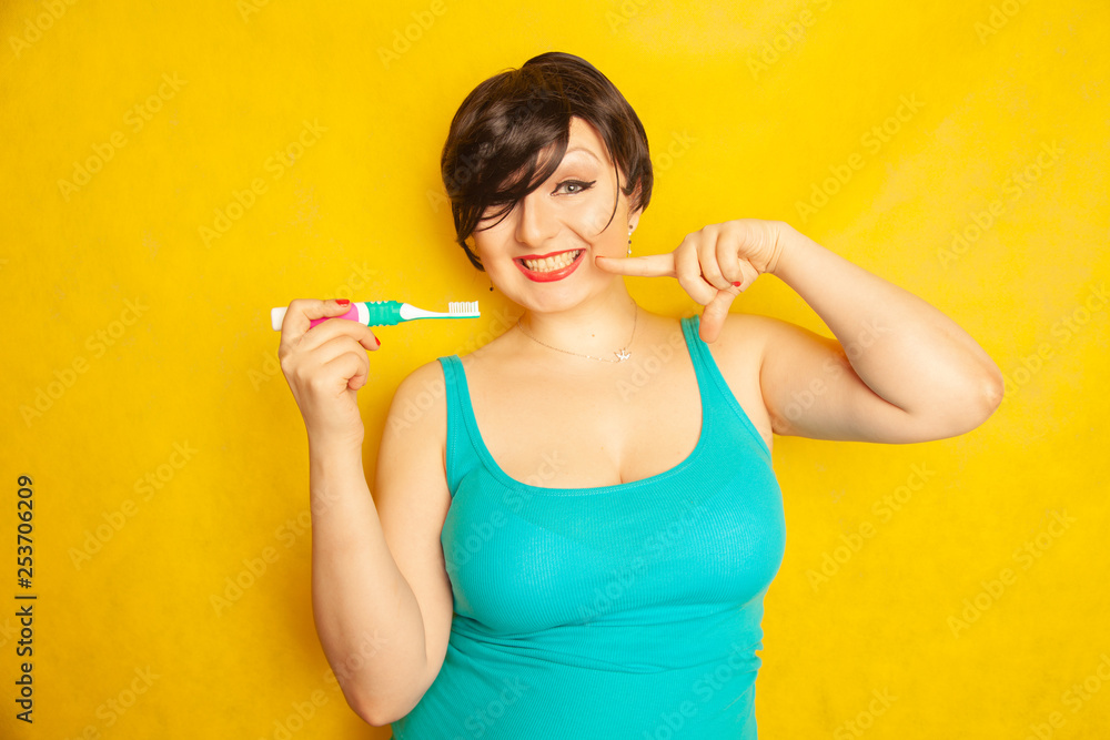 smiling girl with short hair and a curvy figure stands with a toothbrush in her hands on yellow solid studio background smiling girl with short hair and a curvy figure stands with a toothbrush in her hands on yellow solid studio background