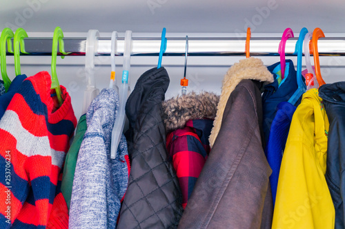 Little boy's child size jackets, coats and sweaters hanging in a kid's closet with colorful hangers.