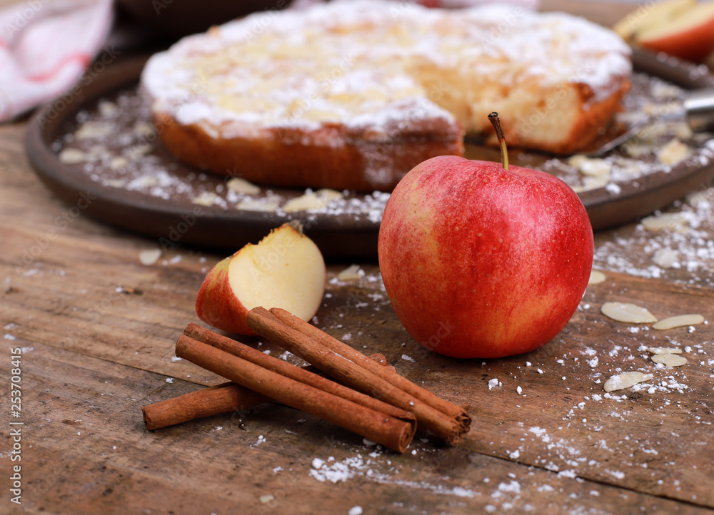 Apple pie - fresh apples and cinnamon sticks in front of a homemade apple pie on a rustic wooden table Apple pie - fresh apples and cinnamon sticks in front of a homemade apple pie on a rustic wooden table