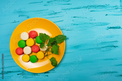 Colorful macaroons on yellow plate on wooden table. Copy space.