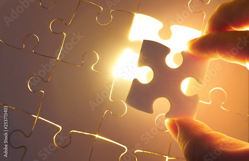 Canvas Print Young businessman trying to put back missing jigsaw puzzle piece with light golden glow effect