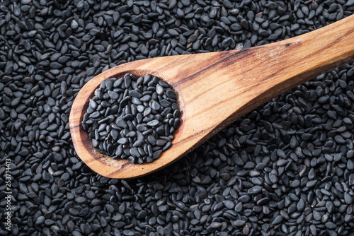 Black sesame seeds in the wooden spoon. Sesame seeds in the dish at the background. Top view. photo