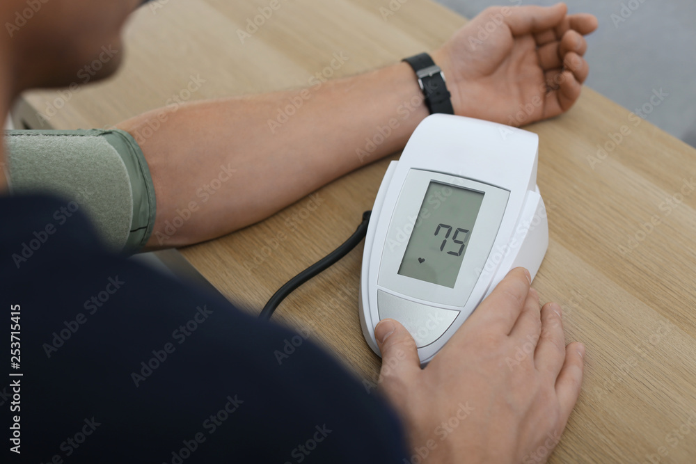 Man checking blood pressure with sphygmomanometer at table indoors, closeup. Cardiology concept Man checking blood pressure with sphygmomanometer at table indoors, closeup. Cardiology concept