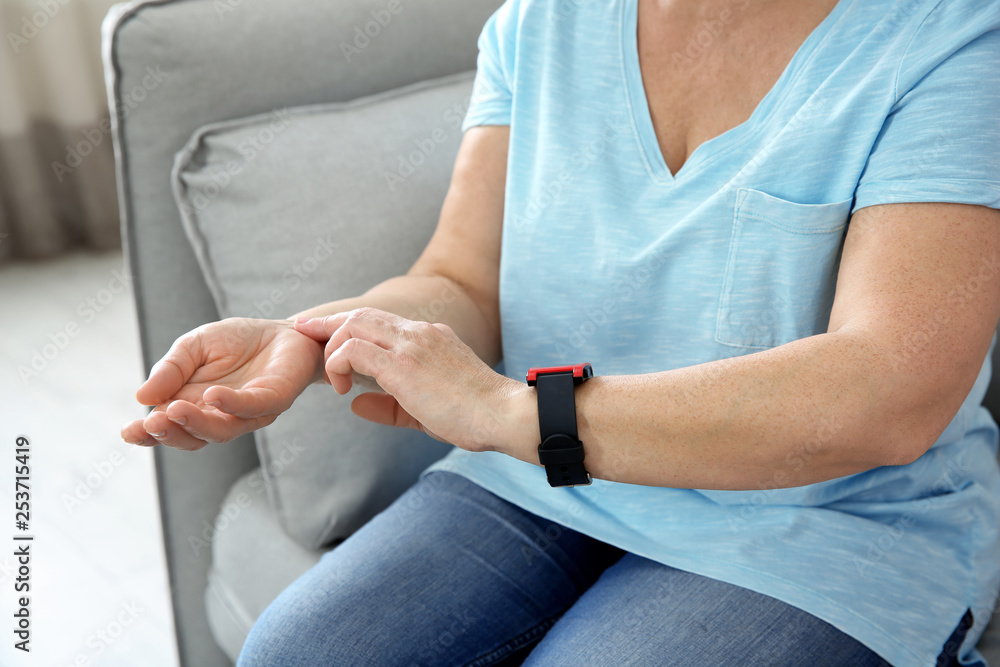 Mature woman checking pulse with fingers at home, closeup