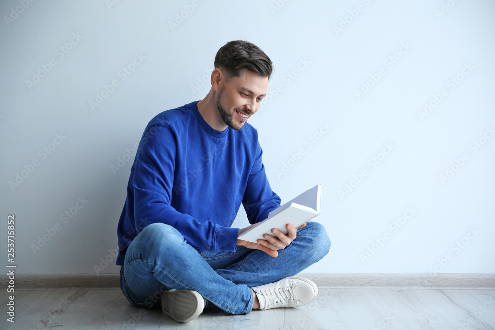 Handsome man reading book on floor near wall, space for text Handsome man reading book on floor near wall, space for text