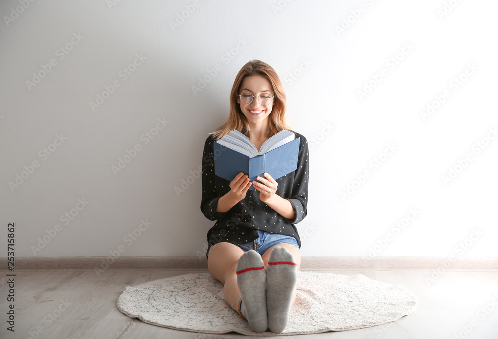 Fototapeta premium Young woman reading book on floor near wall