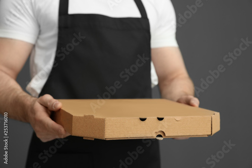 Waiter in apron with pizza box on grey background, closeup. Food delivery service © New Africa