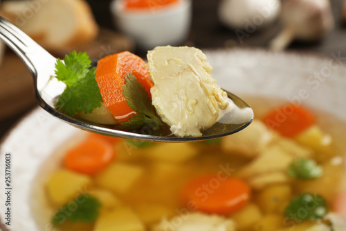 Spoon with fresh homemade chicken soup on blurred background, closeup